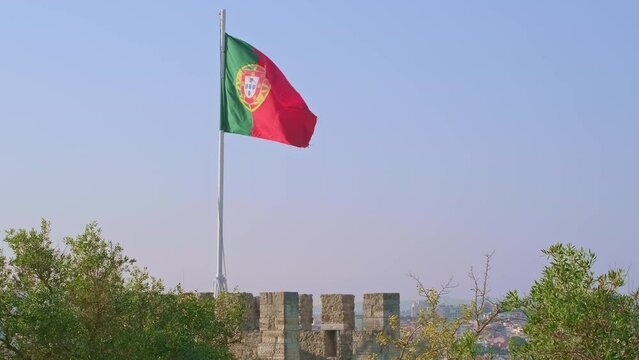 National flag of Portugal waving in the wind on clear sunny day at blue sky over olive trees of Castelo de Sao Jorge. Real footage, Lisbon, Portugal