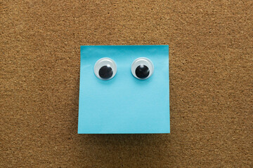 googly eyes on clean blue  sticky note on cork board concept using sticky notes 