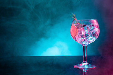 Cold gin tonic under pink and blue light illumination on smoky background with copy space. - obrazy, fototapety, plakaty