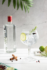 Cold glass of gin tonic and bottle on white wooden base on light background. Vertical format.