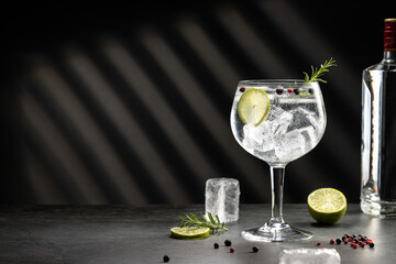 Cold glass of gin tonic with ice and hard shadows on dark gray background with copy space.