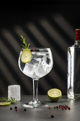Cold glass of gin tonic with ice and hard shadows on dark gray background with copy space. Vertical...