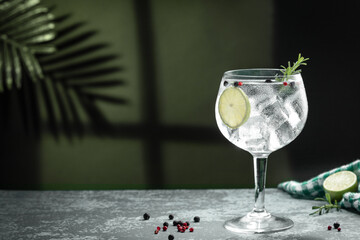 Gin tonic cocktail and shadows next to the window on dark concrete background.