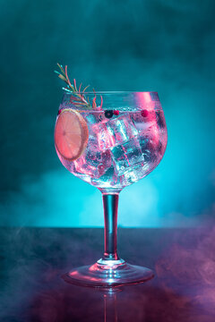 Cold gin and tonic under pink and blue light illumination on smoky background with copy space. Vertical format.