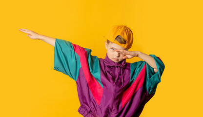 Stylish kid boy in 80s sport suit and cap on yellow background