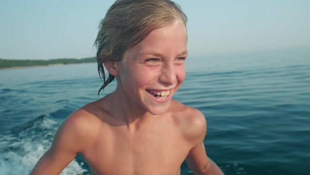 Close up portrait of happy kid riding a boat in the sea during summer vacation, authentic laughter and emotion.