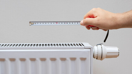 hand holding meter on modern white radiator with thermostat background