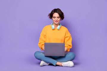 Portrait of attractive cheery focused girl sitting lotus pose using netbook writing email isolated...