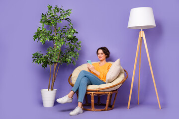 Portrait of attractive cheery focused girl sitting in chair using device rest smm post isolated...