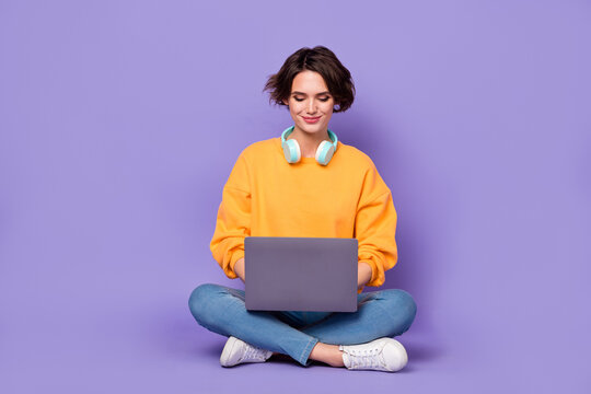 Portrait of attractive cheery focused girl sitting lotus pose using netbook writing email isolated over violet lilac color background