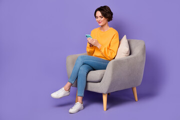 Fototapeta na wymiar Portrait of attractive cheerful trendy girl sitting in chair using gadget 5g post isolated over violet lilac color background
