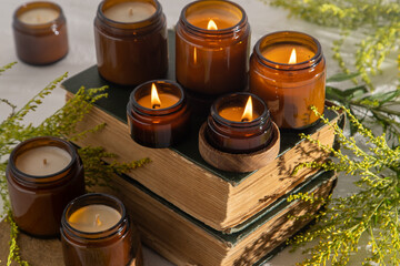 Obraz na płótnie Canvas A set of different aroma candles in brown glass jars. Scented handmade candle. Soy candles are burning in a jar. Aromatherapy and relax in spa and home. Fire in brown jar. Yellow flowers