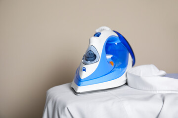 Modern iron and clean shirt on board against beige background, space for text