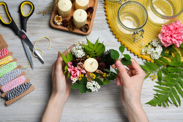 Woman making floral composition with candle at wooden table, top view. Master class in handmade craft