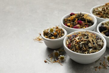 Different dry aromatic teas on light grey table, space for text