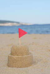 Fototapeta na wymiar Beautiful sand castle with red flag on beach near sea