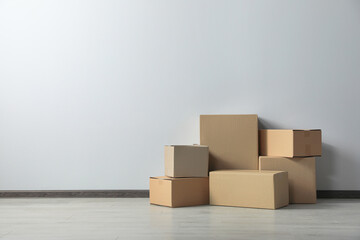 Many closed cardboard boxes on floor near white wall, space for text. Delivery service
