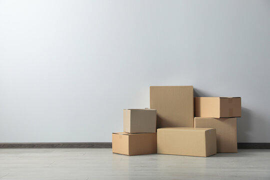 Many closed cardboard boxes on floor near white wall, space for text. Delivery service