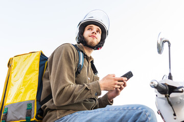 Portrait of a courier on a scooter with a yellow bag. The deliverer looks at the address of the...