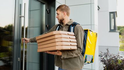 The courier opens the entrance door to deliver pizzas to the customer. The man works in the field...