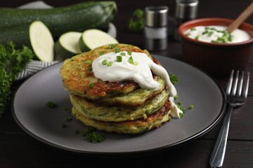 Delicious zucchini fritters with sour cream on wooden table