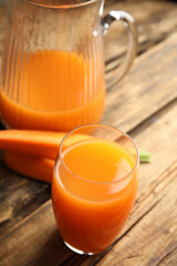 Jug and glass of freshly made carrot juice on wooden table
