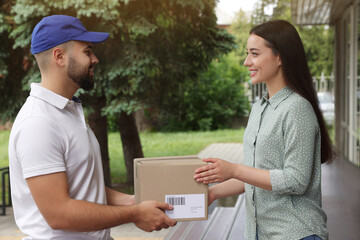 Woman receiving parcel from courier outdoors. Delivery service - obrazy, fototapety, plakaty