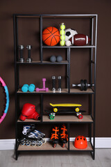 Shelving unit with different sports equipment near brown wall indoors