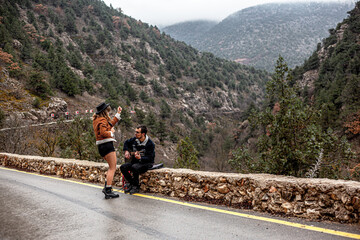 back view of couple in love walking in the countryside road against the mountain and road, man holding the guitar, people hitchhiking . A man gently hugs a woman