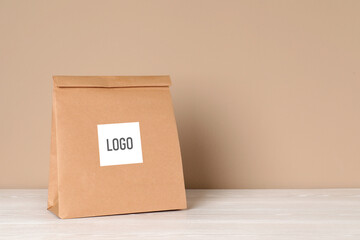 Paper bag with logo on table against beige background. Space for text