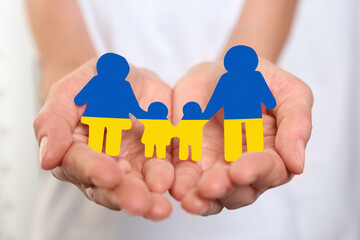 Young woman holding paper family figure in colors of Ukrainian flag, closeup of hands
