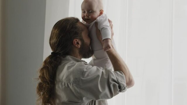 Caucasian Bearded Adult Father Throw Up Little Cute Smiling Son Daughter Infant Playing Together At Home Tickling Tummy Of Baby With Nose Dad Holding Newborn Having Fun With Kid Child Tickle Game