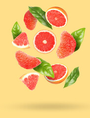 Tasty ripe grapefruits and green leaves falling on beige background