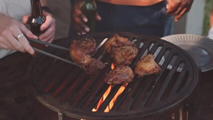 Tilt up slowmo of two multiethnic male friends chatting while cooking meat on bbq grill during backyard party