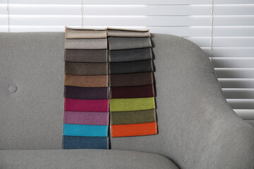 Catalog of colorful fabric samples on grey sofa indoors