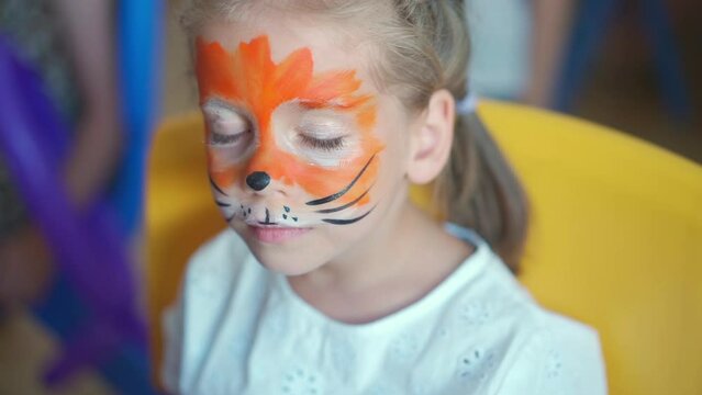 Children face painting. Artist painting with brash and special body paint tiger mask on face of little girl on carnival party for children. Body art painting for childrens.