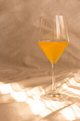 Orange juice in an elegant wine glass on a sunlit white sheet. Romantic aesthetic. Natural sunlight and shadows.
