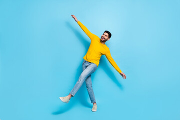 Full length photo of fooling funky man wear yellow sweater walking arms sides isolated blue color...