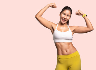 Shot of smiling young sporty Asian woman fitness model in white-top sportswear showing hand biceps muscles isolated on pastel plain light pink background. Fitness and healthy lifestyle concept.