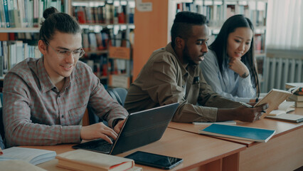 Obraz premium Multi ethnic group concentrated students talking and preparing for examination while sitting at the table in university library indoors