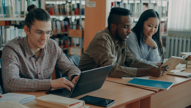 Multi ethnic group concentrated students talking and preparing for examination while sitting at the table in university library indoors