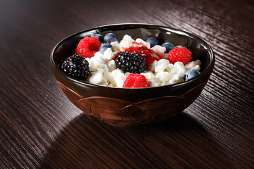 Grain cottage cheese with ripe berries fresh raspberries and blueberries and blackberries in a clay bowl for a healthy breakfast on a wooden background. Close-up, selective focus.