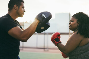 African curvy woman and personal trainer doing boxing workout session outdoor - Focus on woman face