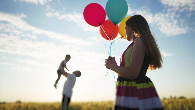 happy family celebrates birthday in the park. girl a holding colorful balloons silhouette in the field. dad throws his son into the sky lifestyle in the park. happy family kid dream concept