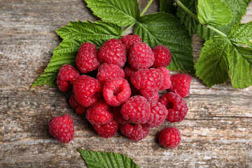 Fresh ripe raspberries and green leaves on wooden table, flat lay