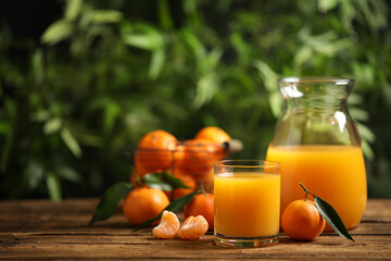 Glass and bottle of fresh tangerine juice and fruits on wooden table. Space for text