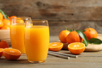 Glasses of fresh tangerine juice and fruits on wooden table. Space for text
