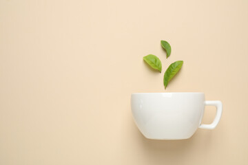 Fresh tea leaves and cup on beige background, top view. Space for text