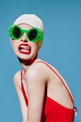 A grimacing girl in a swimming cap and a red swimsuit sticks out her glasses