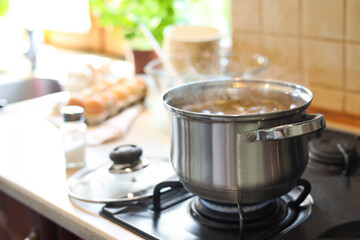 Shiny pot with boiling water on stove indoors. Space for text